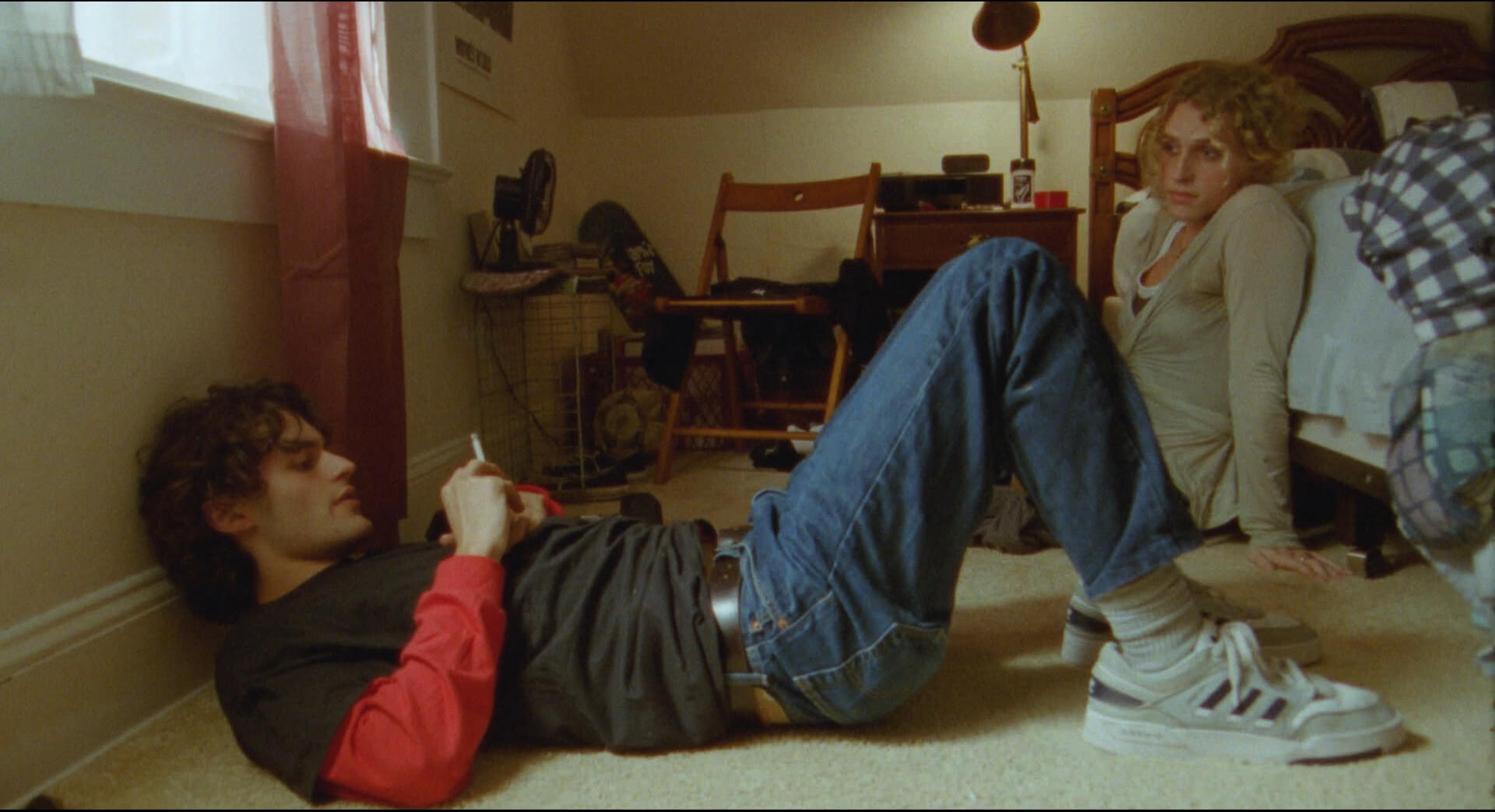 Molly and Tom sit on the floor of tom's room. Tom is laying on the ground with a cigarette; Molly is sitting on the floor, leaning against the bed.