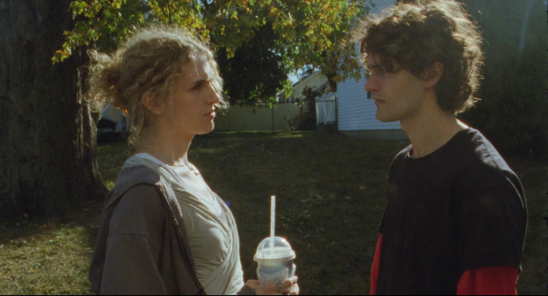 Molly and Tom stand face to face in front of a suburban front yard on a sunny day.