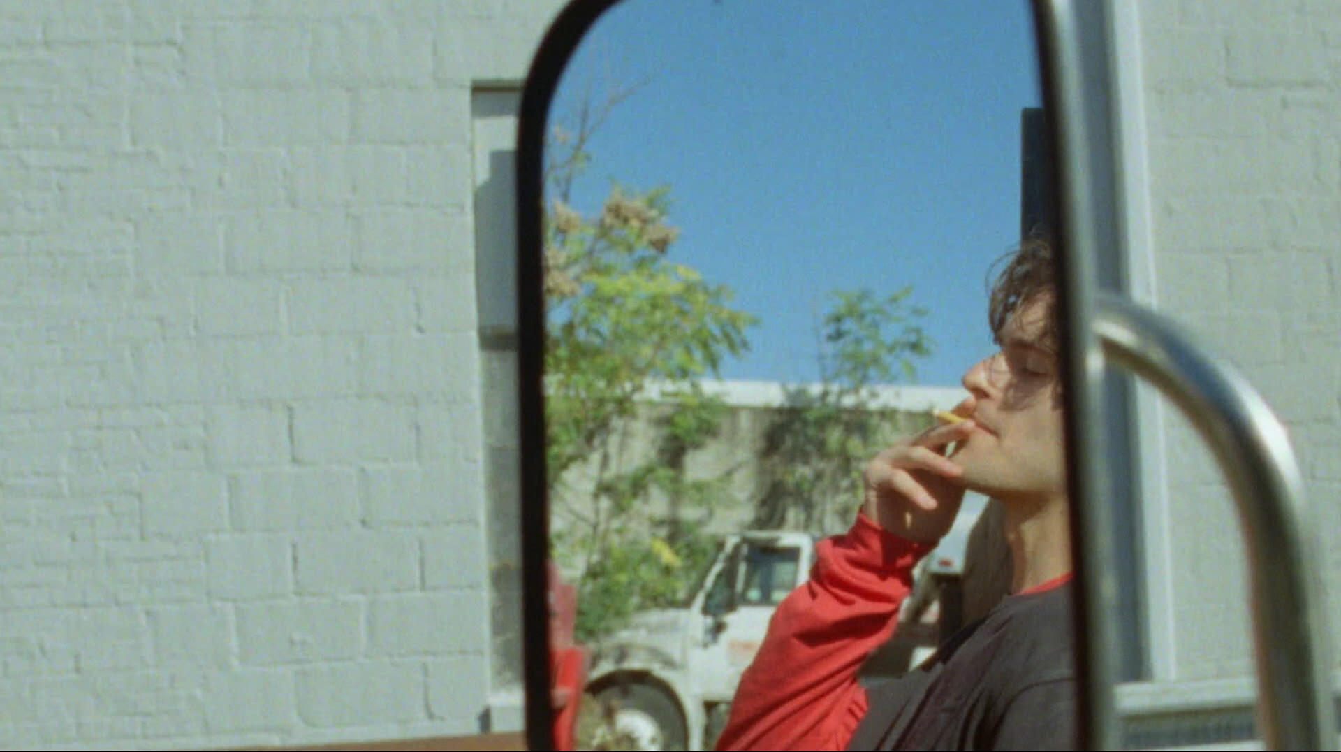 Tom, reflected in the mirror of a truck, smoking a cigarette.
